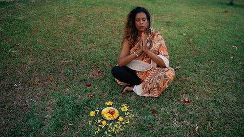 A Woman Doing Rituals While Sitting on a Grass Field