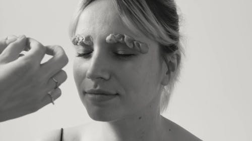 Person Sticking Petals on Woman's Eyebrows