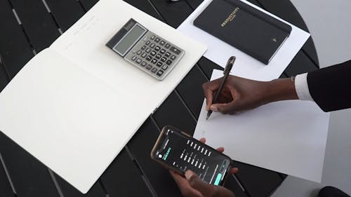 Man Holding Cellphone Writing on a Paper