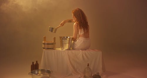 A Woman Pouring Water into a Metal Bucket