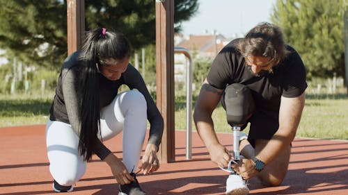 A Woman and a Man with Prosthetic Leg Tying Their Shoes