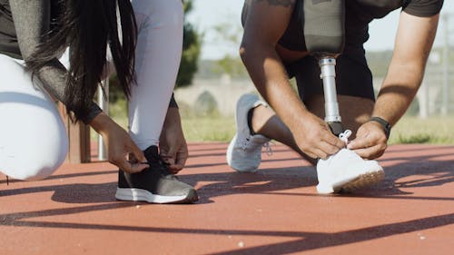 A Woman and a Man with Prosthetic Leg Tying Their Shoes