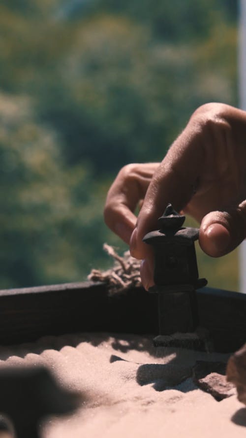 A Person Placing a Figurine in a Mini Zen Garden