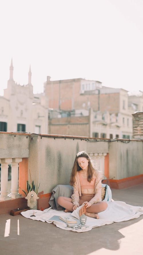 A Woman Sitting on the Rooftop while Reading a Book