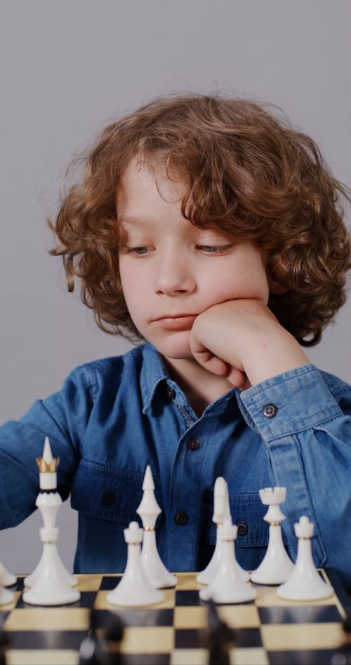 A Boy Thinking His Next Move While Holding a Chess Piece