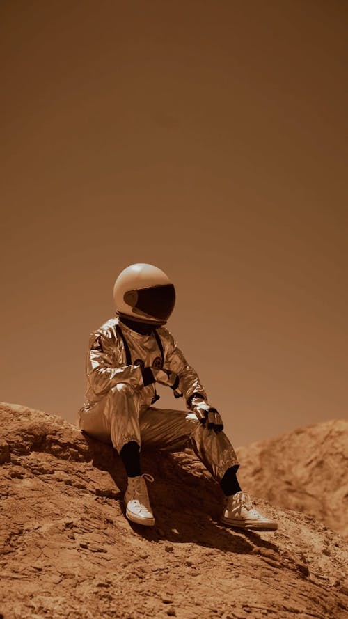 An Astronaut Sitting and Looking Around in a Desert