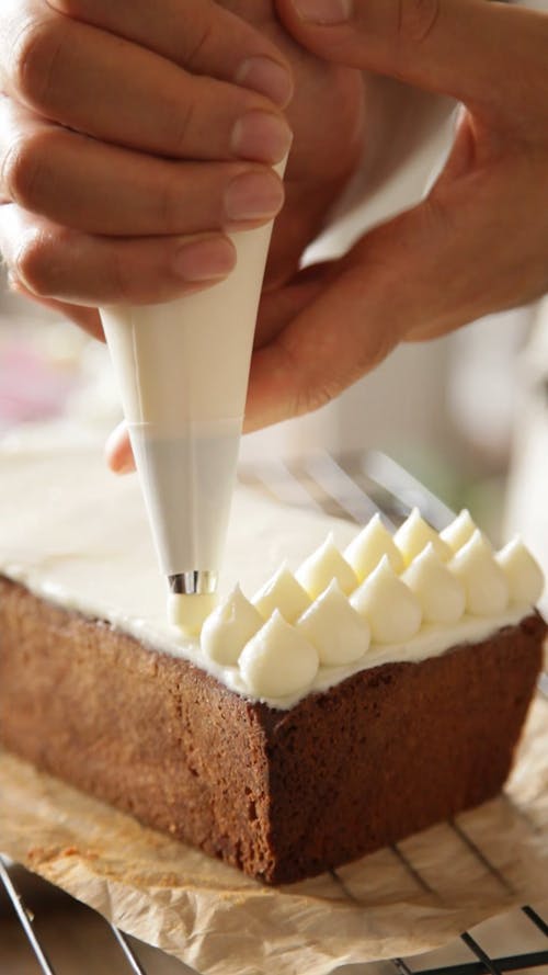 A Person Putting Icing on the Top of a Cake