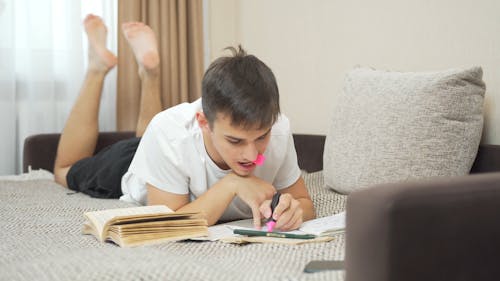 Man Lying on Bed Doing Assignment