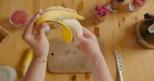 A Person Placing a Peeled Banana on a Wooden Chopping Board