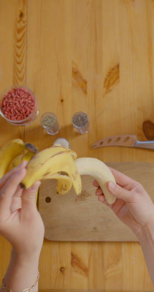A Person Placing a Banana on a Wooden Chopping Board