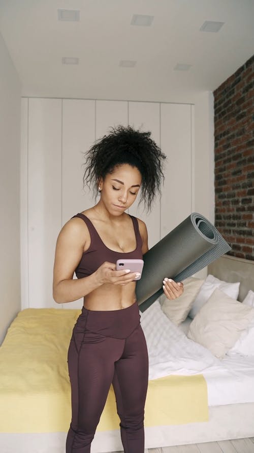 Woman Holding Yoga Mat While Using a Cellphone