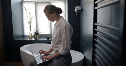 A Woman Using Laptop in a Bathroom