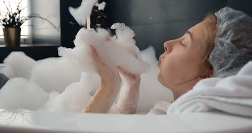 Woman Blowing Bubbles While In the Bath Tub