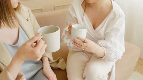 Women Talking and Having Coffee while Sitting on a Couch