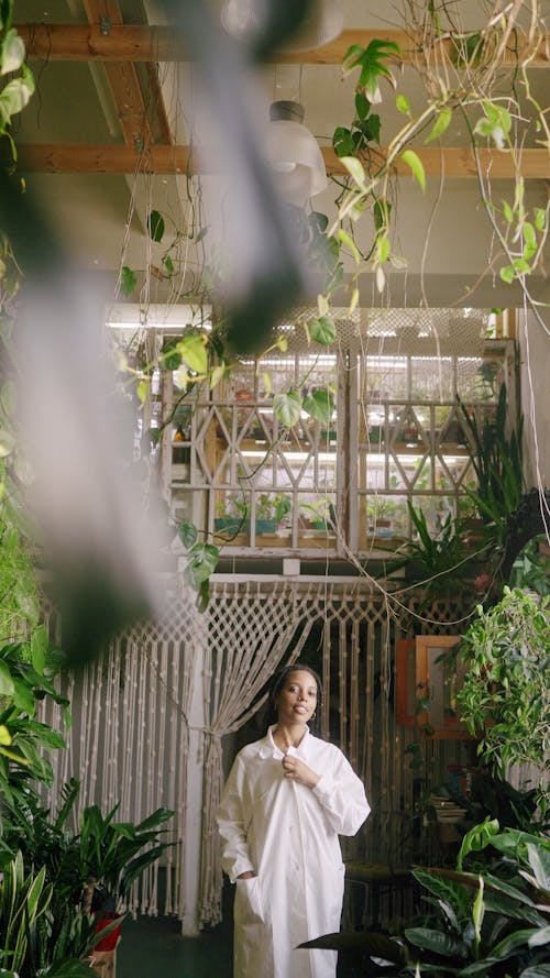 A Woman in a Lab Coat Standing in a Room Full of Plants