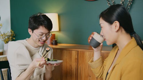 A Man Eating Sushi and a Woman Drinking from a Cup