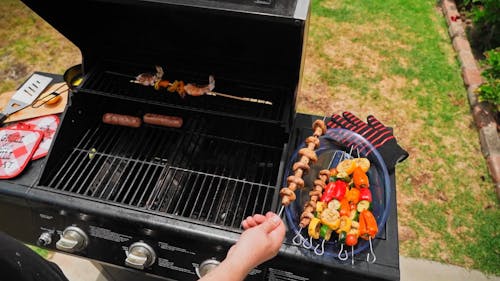 Person Grilling Sausages and Skewers