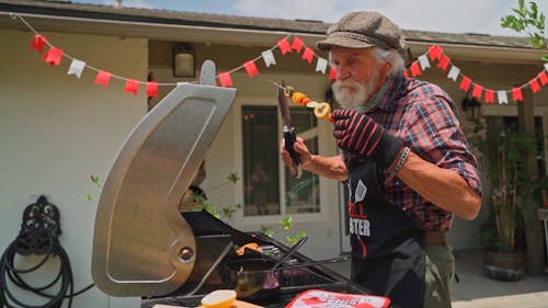 Elderly Man Grilling Vegetables and a Hot Dog
