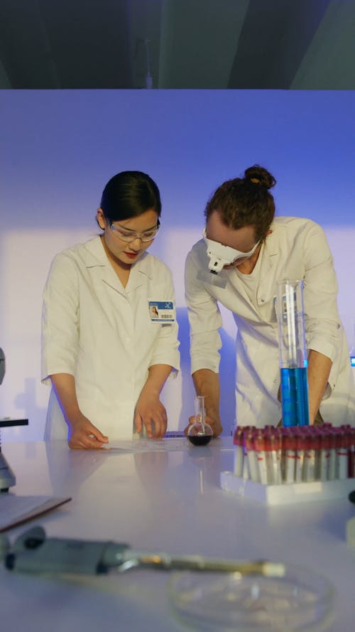 A Male and Female Scientist Looking at Notes in a Lab