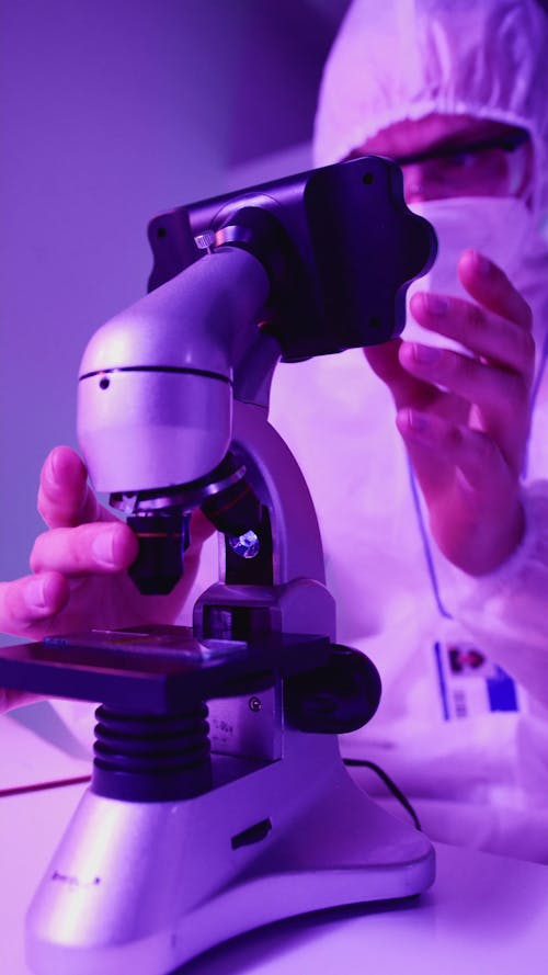 A Person Wearing a PPE Suit Adjusting a Microscope