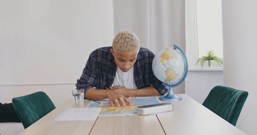 A Young Man Taking Notes after Looking at a Map and a Globe