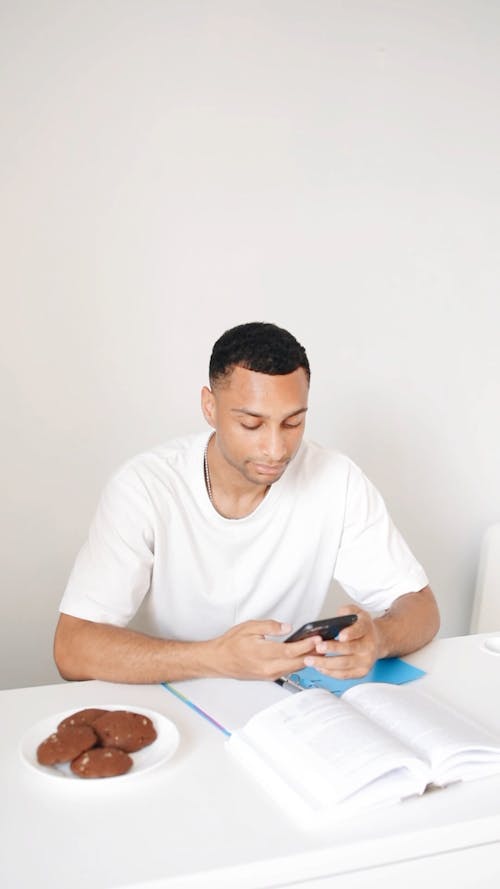 A Young Man Using his Cellphone while Studying