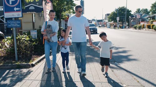 A Family Holding Each Other's Hands while Walking on the Sidewalk