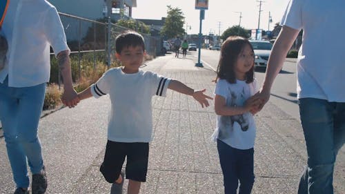 A Family Holding Each Other's Hands while Walking on the Sidewalk
