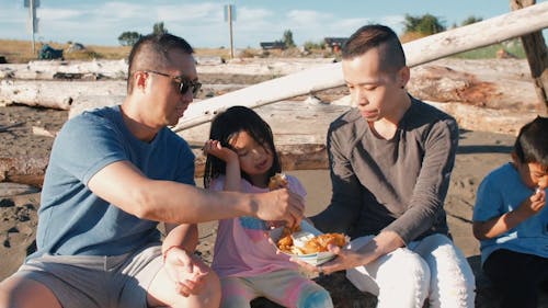 Family Sitting on a Log while Eating Snacks