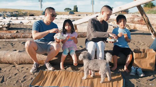 Family Sitting on a Log while Eating Snacks