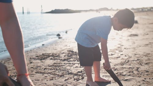 Boy Writing on Beach Sand Using a Stick