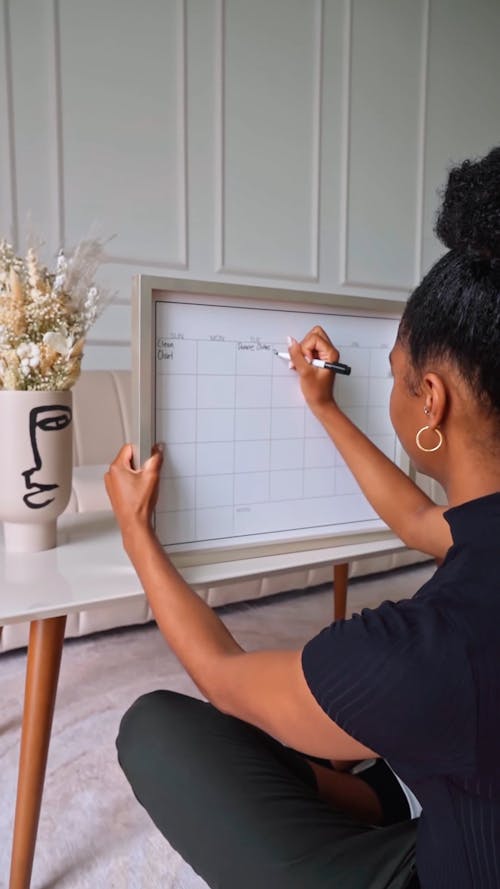 Woman Writing on a Whiteboard Planner while Sitting on the Floor