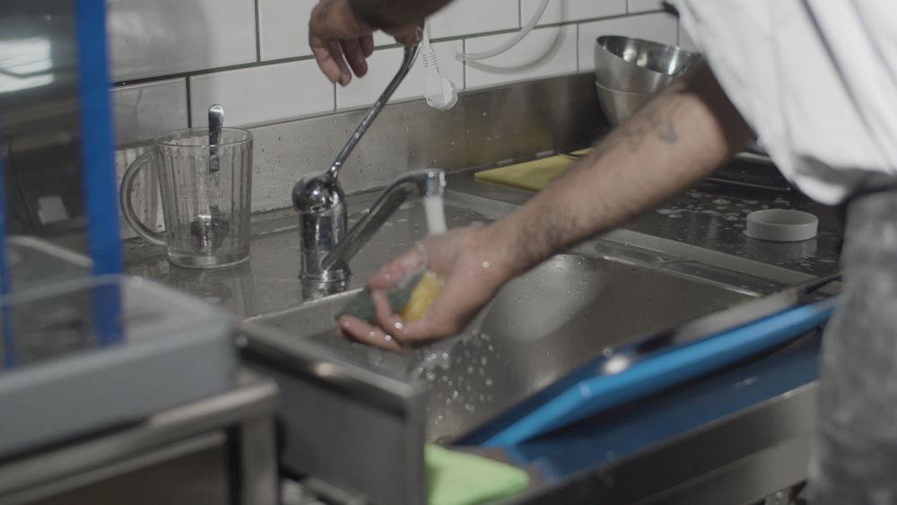 Kitchen worker washing utensils at a commercial sink
