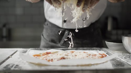 Close up of a Chef Sprinkling Grated Cheese on a Pizza