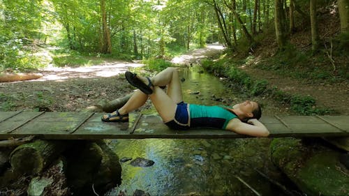 A Woman Relaxing in the Forest while Lying on a Wooden Pathway