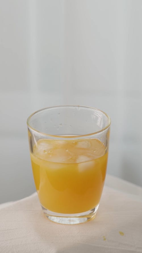Ice Being Dropped into a Glass of Fruit Juice