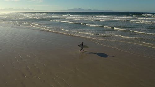 A Person Running at the Beach while Surfing