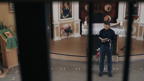 A Man Standing in Front of the Altar while Reading a Bible