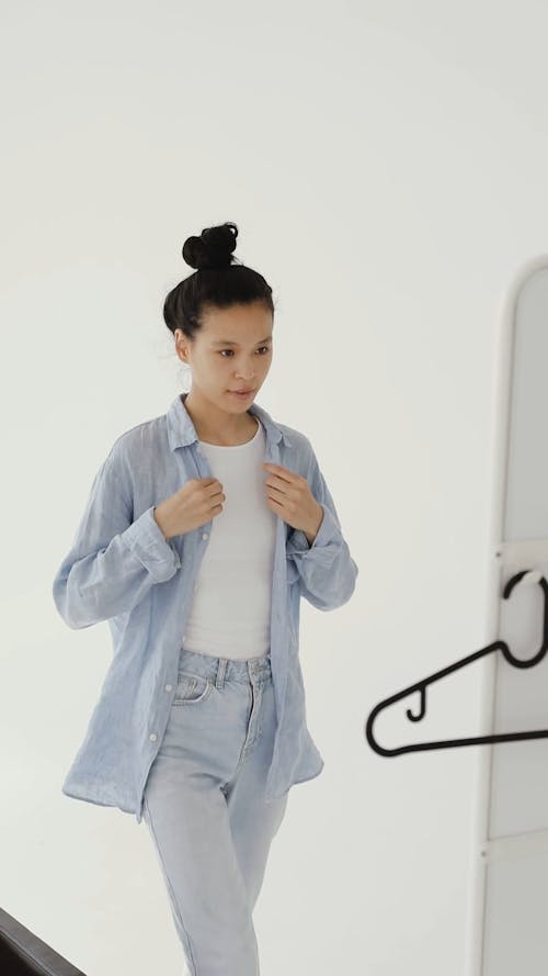 A Woman Looking in a Mirror while Buttoning her Shirt