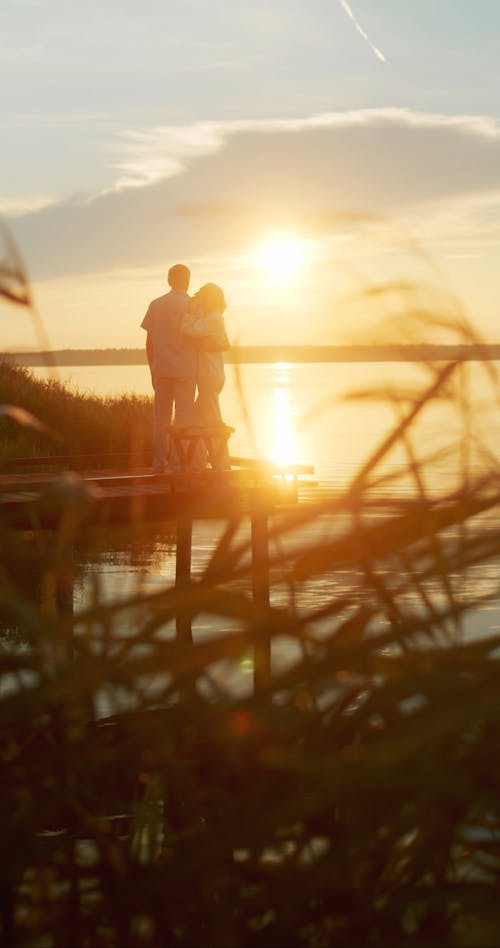 Back View of a Couple Standing on a Dock at Sunset