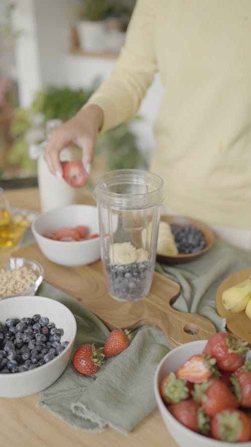 A Person Putting Different Kind of Fruits in a Blender