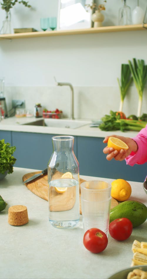 Person Squeezing Lemon on a Container with Water 