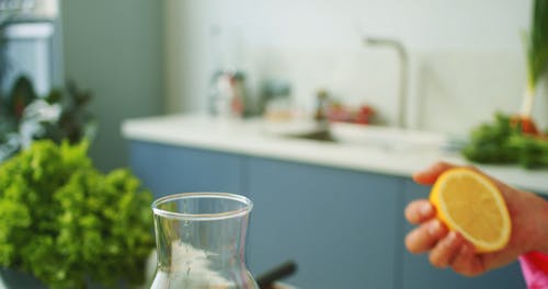 A Person Squeezing a Lemon into a Glass Pitcher