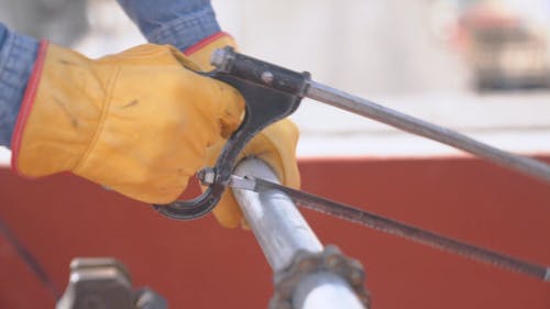 Man Wearing Gloves Sawing A Steel Pipe