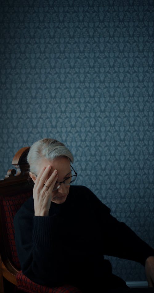 An Elderly Woman Taking off her Eyeglasses while Sitting in an Armchair