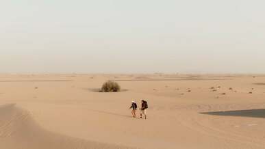 a man and woman walking on an asphalt road built on a desert