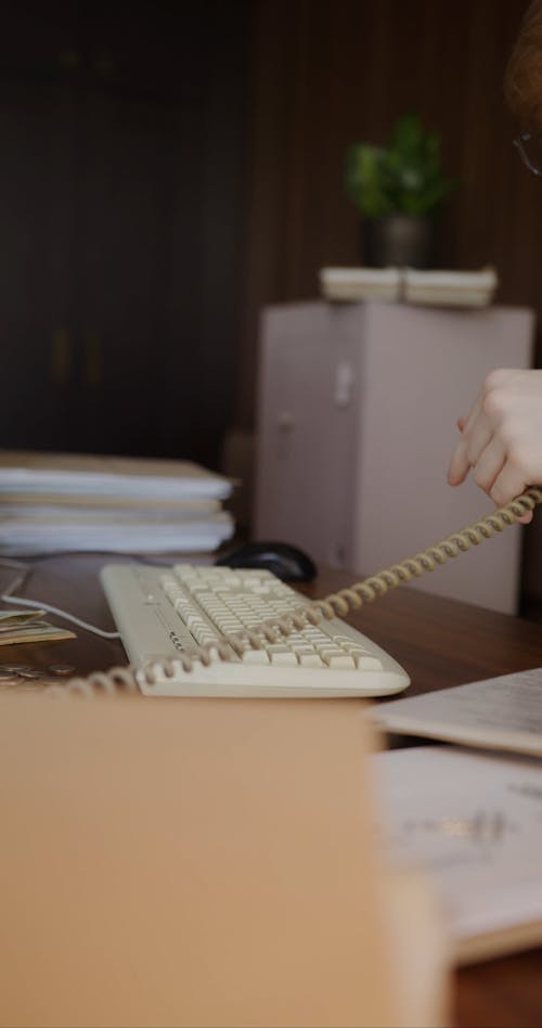 A Man Talking on the Phone while Typing on a Keyboard