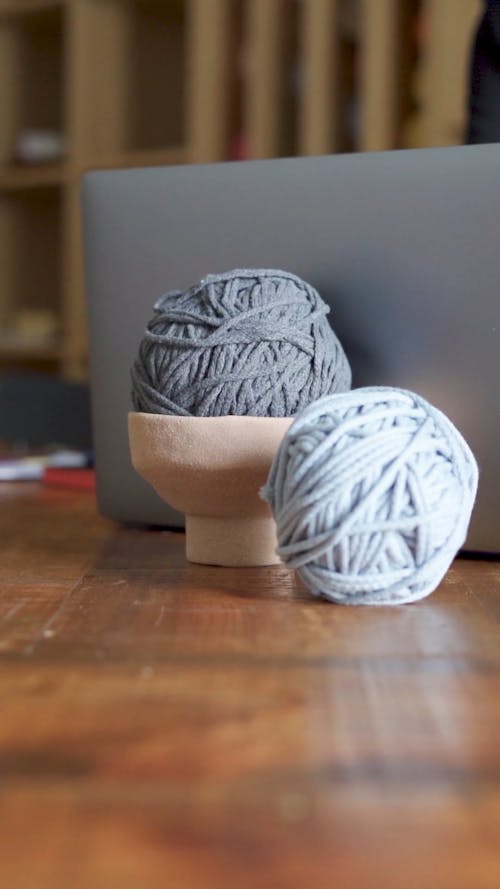 Two Balls Of Yarn behind a Laptop at a Table