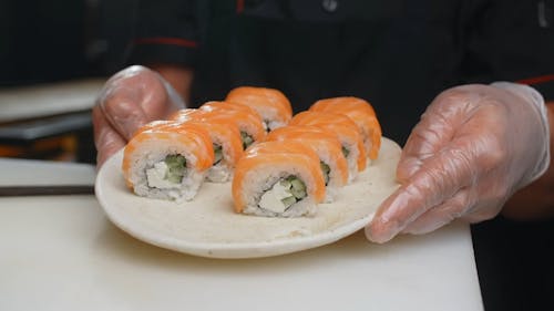A Person Holding a Plate of Salmon Sushi Rolls