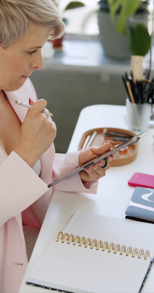 A Woman Sketching on Notebook while Looking on Tablet